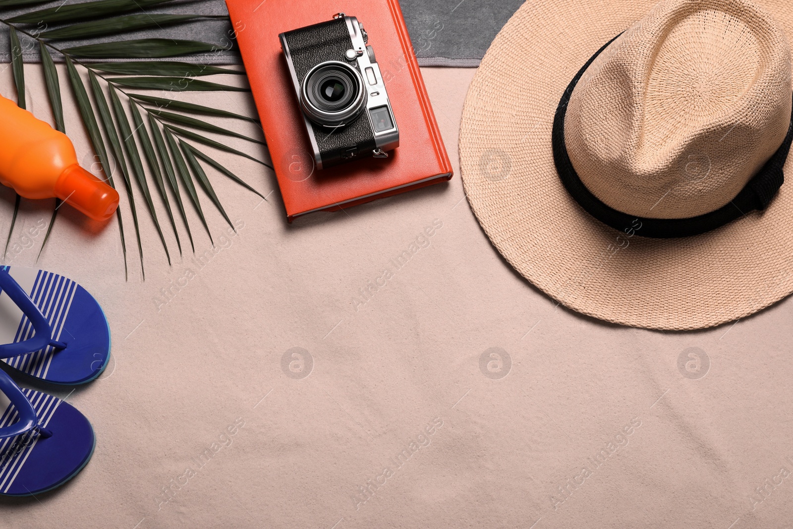 Photo of Beach towel, hat, book, camera, sunscreen, flip flops and tropical leaf on sand, flat lay. Space for text