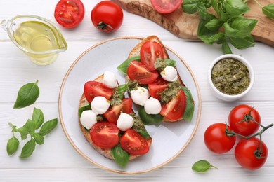 Photo of Delicious Caprese sandwiches with mozzarella, tomatoes, basil and pesto sauce on white wooden table, flat lay