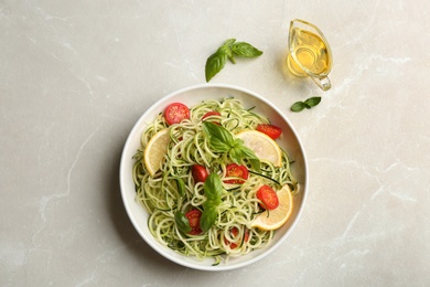 Photo of Delicious zucchini pasta with cherry tomatoes, lemon and basil served on light grey table, flat lay