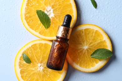 Photo of Bottle of cosmetic serum, orange slices and green leaves on light blue background, flat lay