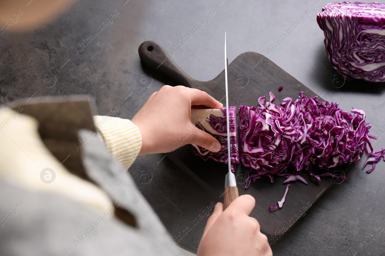 Photo of Woman cutting fresh red cabbage at black table, closeup