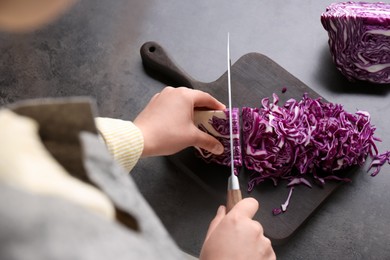 Woman cutting fresh red cabbage at black table, closeup