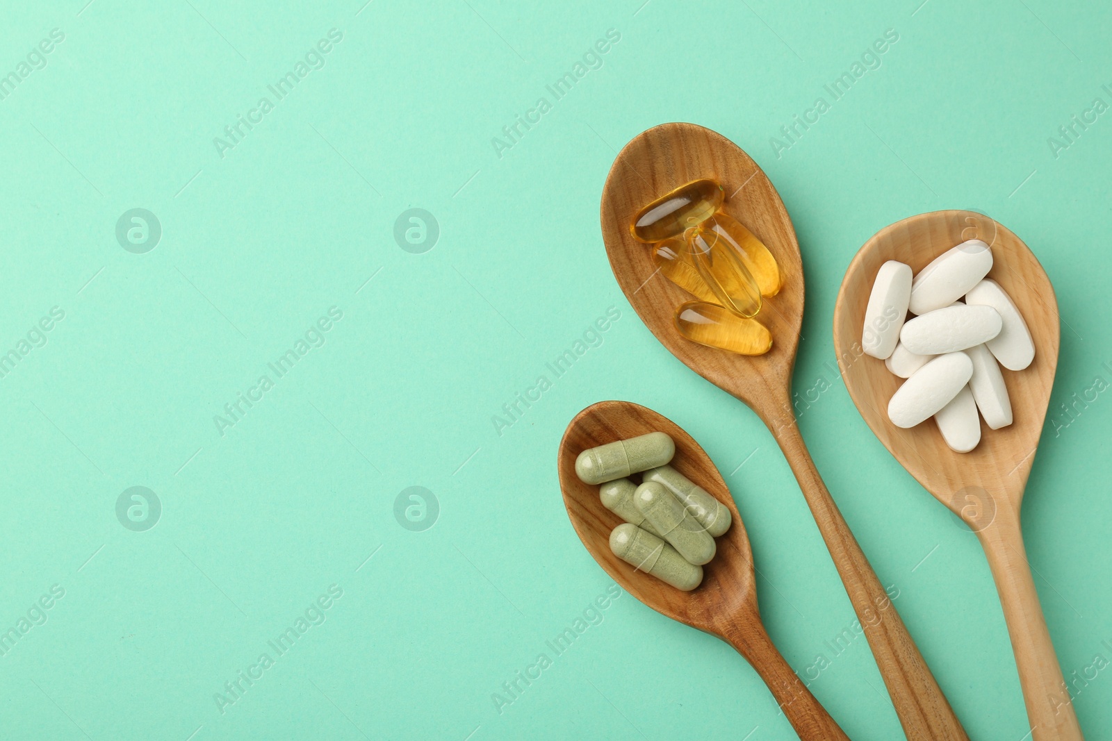 Photo of Different vitamin capsules in spoons on turquoise background, flat lay. Space for text