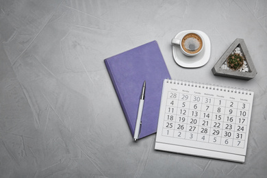 Flat lay composition with calendar and cup of coffee on grey table. Space for text