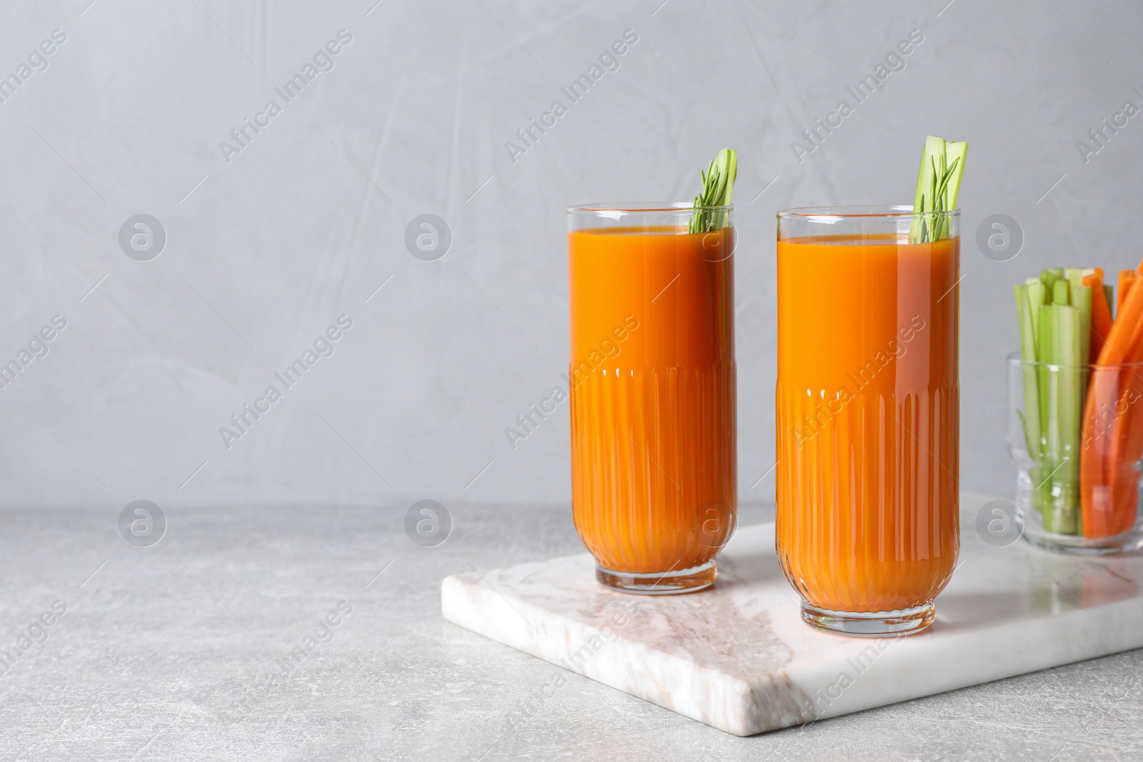 Photo of Glasses of tasty carrot juice with celery sticks on light grey table, space for text