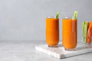 Glasses of tasty carrot juice with celery sticks on light grey table, space for text