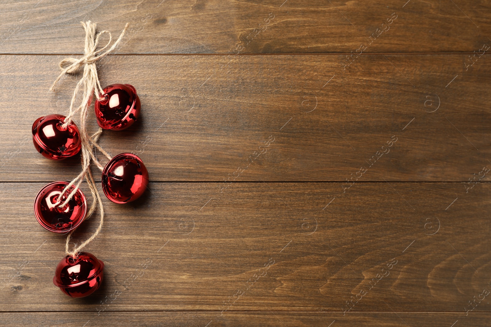 Photo of Shiny red sleigh bells on wooden table, top view. Space for text