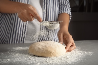 Photo of Woman sprinkling dough for pastry with flour on table