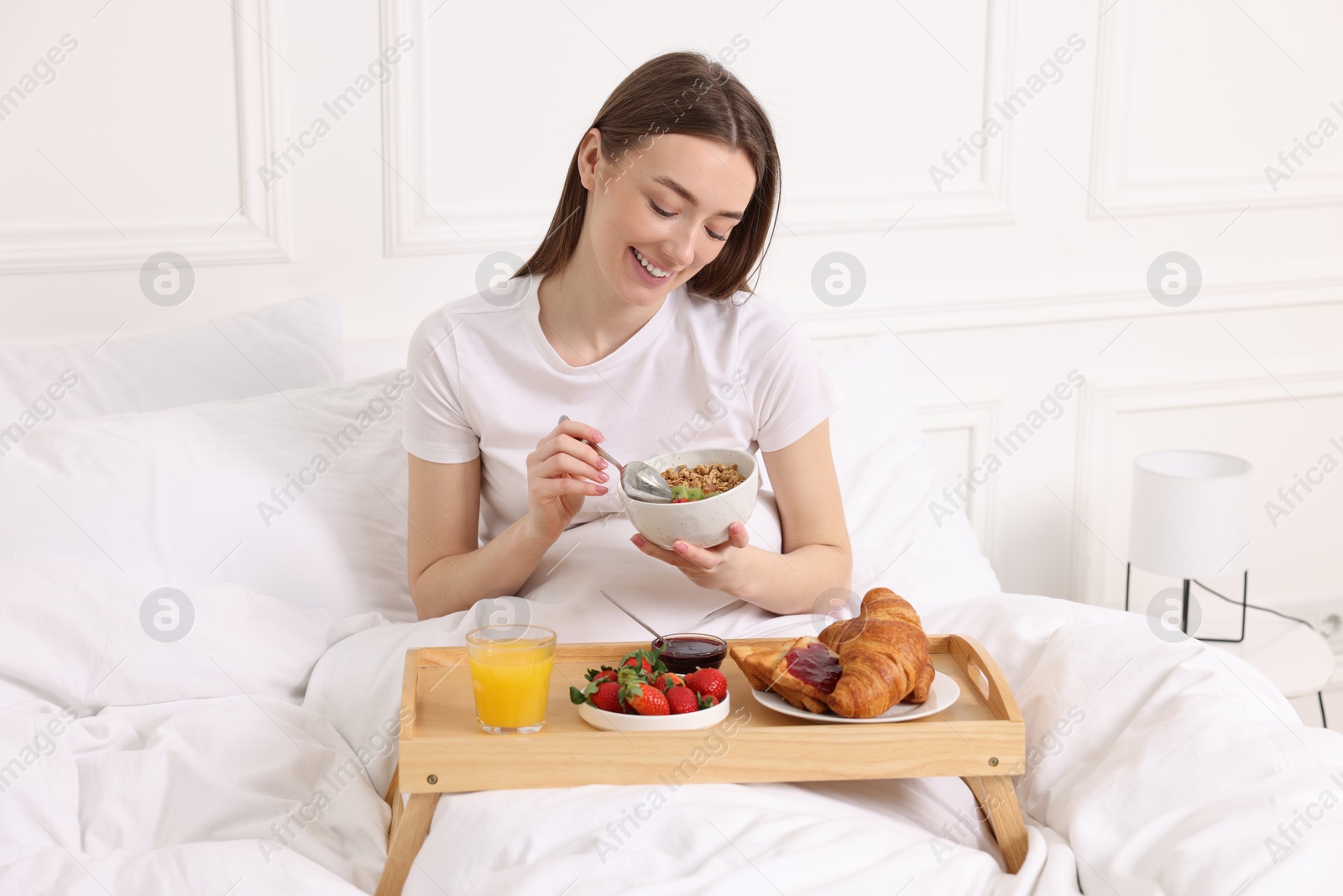 Photo of Smiling woman having tasty breakfast in bed at home