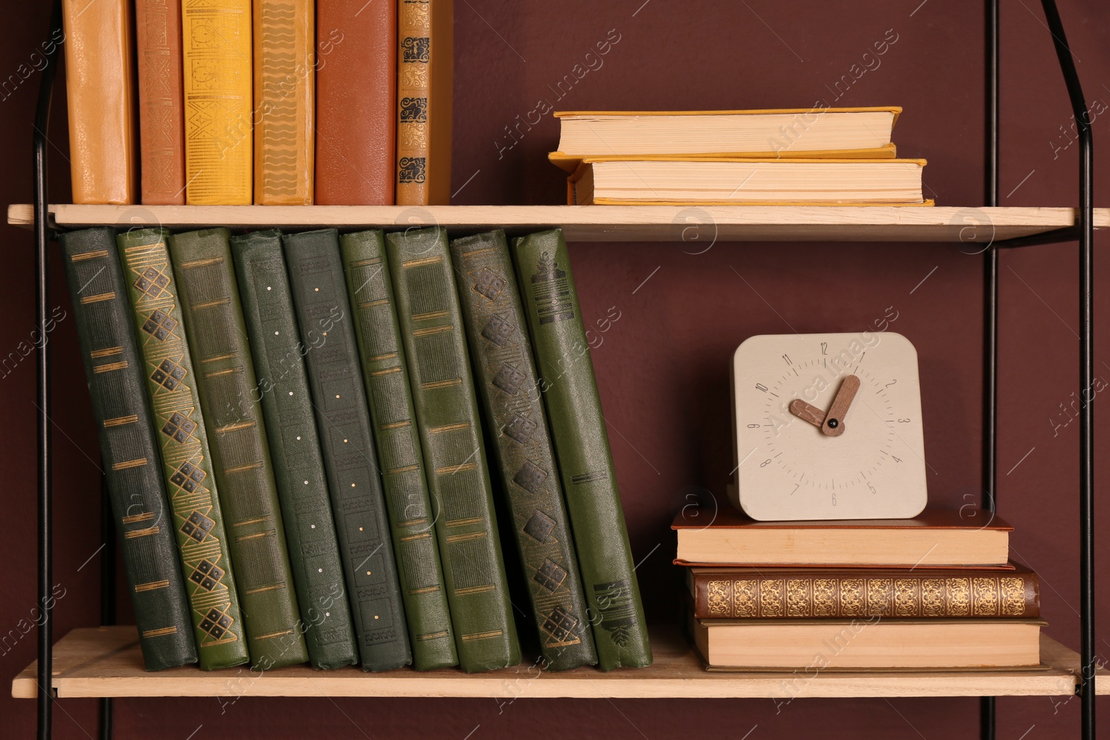 Photo of Shelves with different books and clock on brown wall