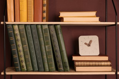 Shelves with different books and clock on brown wall