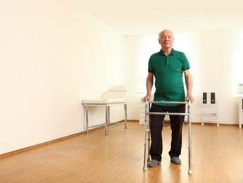 Photo of Elderly man using walking frame indoors. Space for text