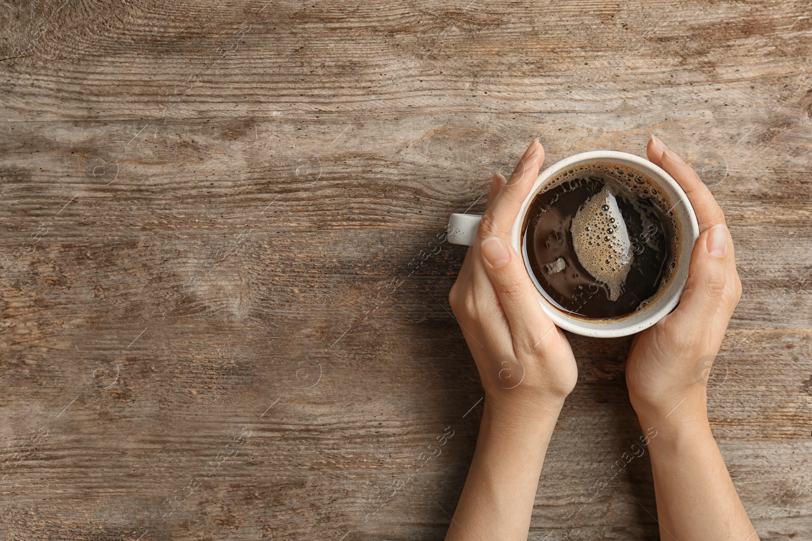Photo of Young woman with cup of delicious hot coffee on wooden background, top view