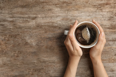 Photo of Young woman with cup of delicious hot coffee on wooden background, top view