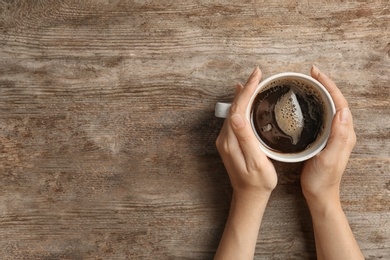 Young woman with cup of delicious hot coffee on wooden background, top view