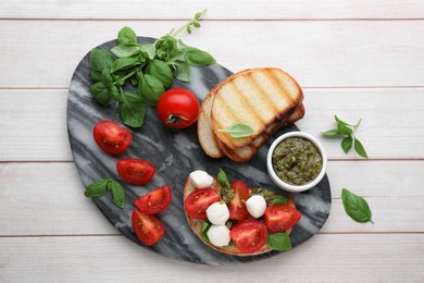 Photo of Delicious Caprese sandwich with mozzarella, tomatoes, basil and pesto sauce on white wooden table, top view