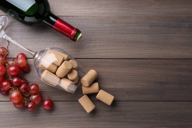 Bottle of wine, glass with corks and grapes on wooden table, flat lay. Space for text