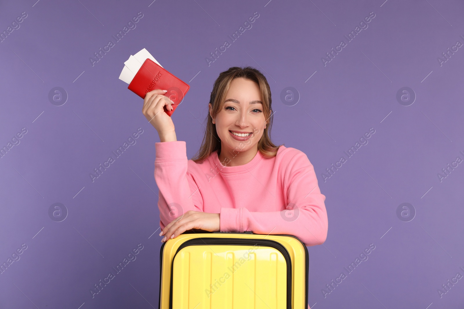 Photo of Happy young woman with passport, ticket and suitcase on purple background