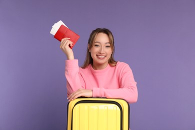 Photo of Happy young woman with passport, ticket and suitcase on purple background