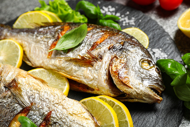 Photo of Delicious roasted fish with lemon on slate plate, closeup