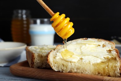 Photo of Pouring honey from dipper onto slices of bread with butter on grey wooden table, closeup