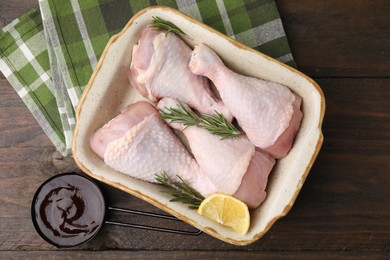 Marinade, raw chicken drumsticks, rosemary and lemon on wooden table, flat lay