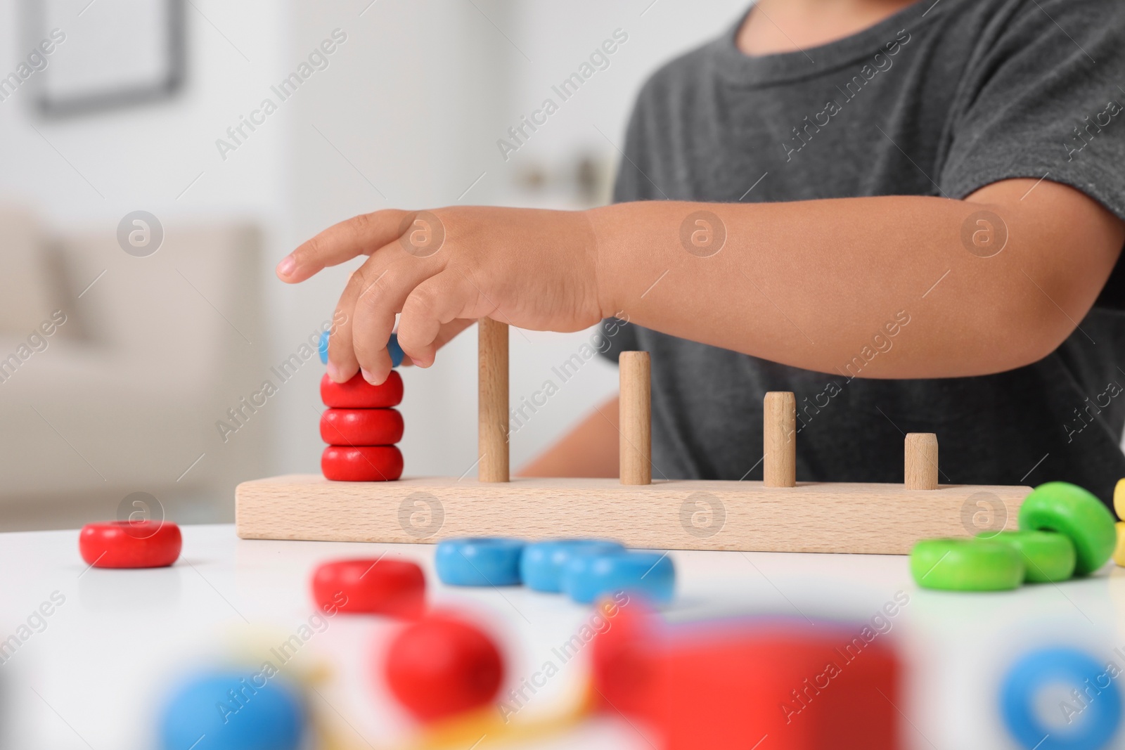 Photo of Motor skills development. Little boy playing with stacking and counting game at table indoors, closeup