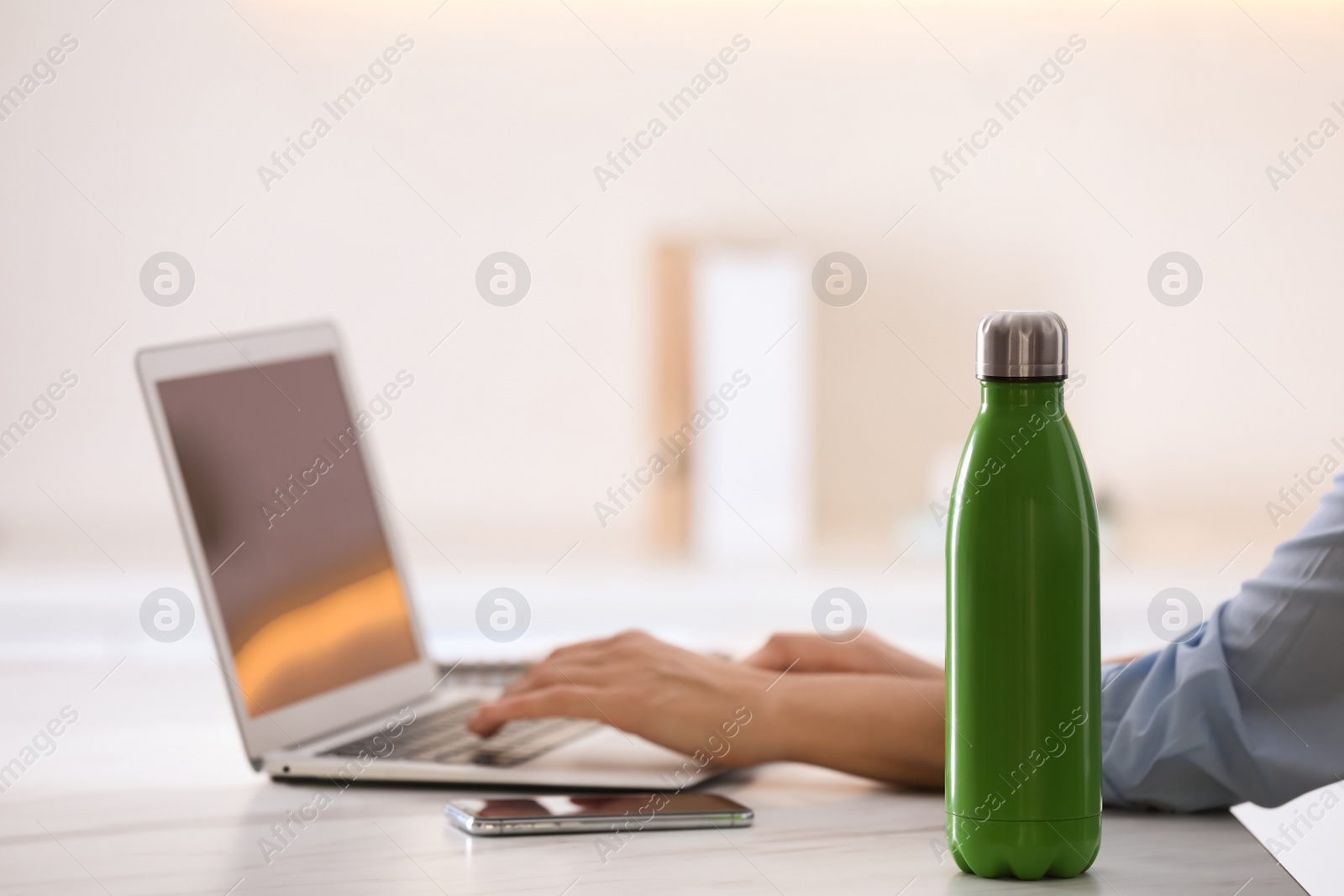 Photo of Woman with thermo bottle working at table in modern office, closeup