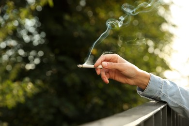Woman smoking cigarette near railing outdoors, closeup of hand. Space for text