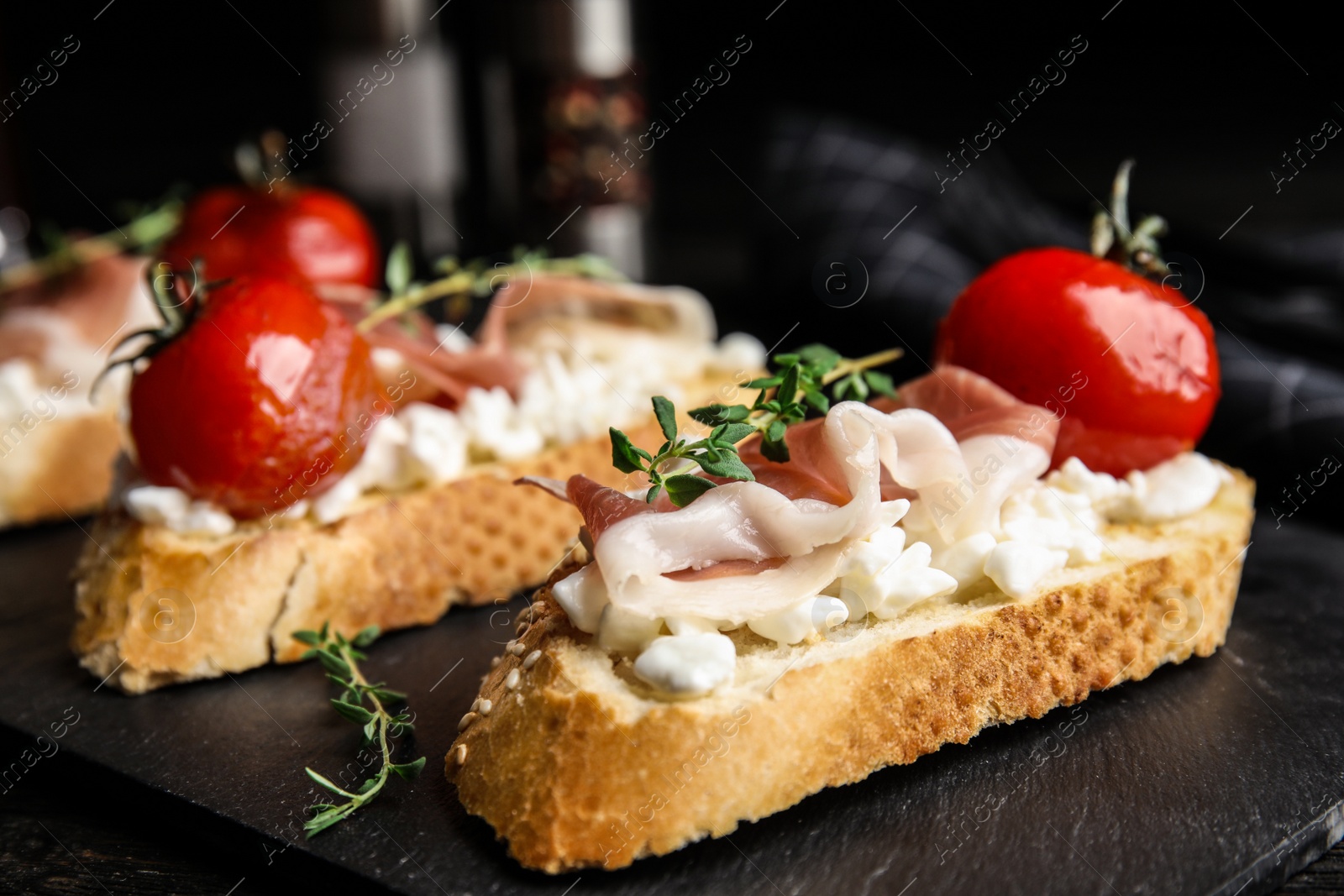 Photo of Slate plate of delicious bruschettas with prosciutto on black wooden table