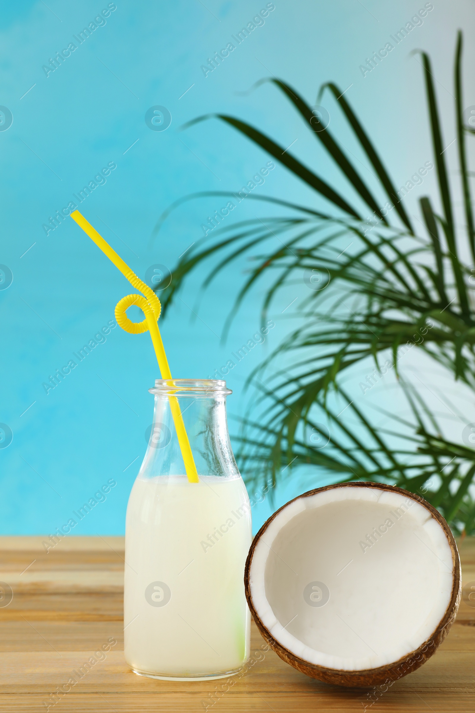 Photo of Composition with bottle of coconut water on wooden table against blue background