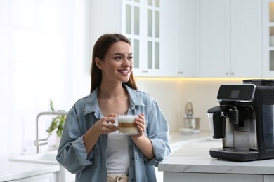 Photo of Young woman enjoying fresh aromatic coffee near modern machine in kitchen