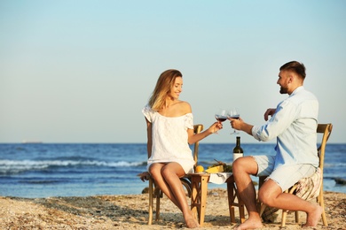Photo of Young couple with glasses of wine having romantic dinner on beach