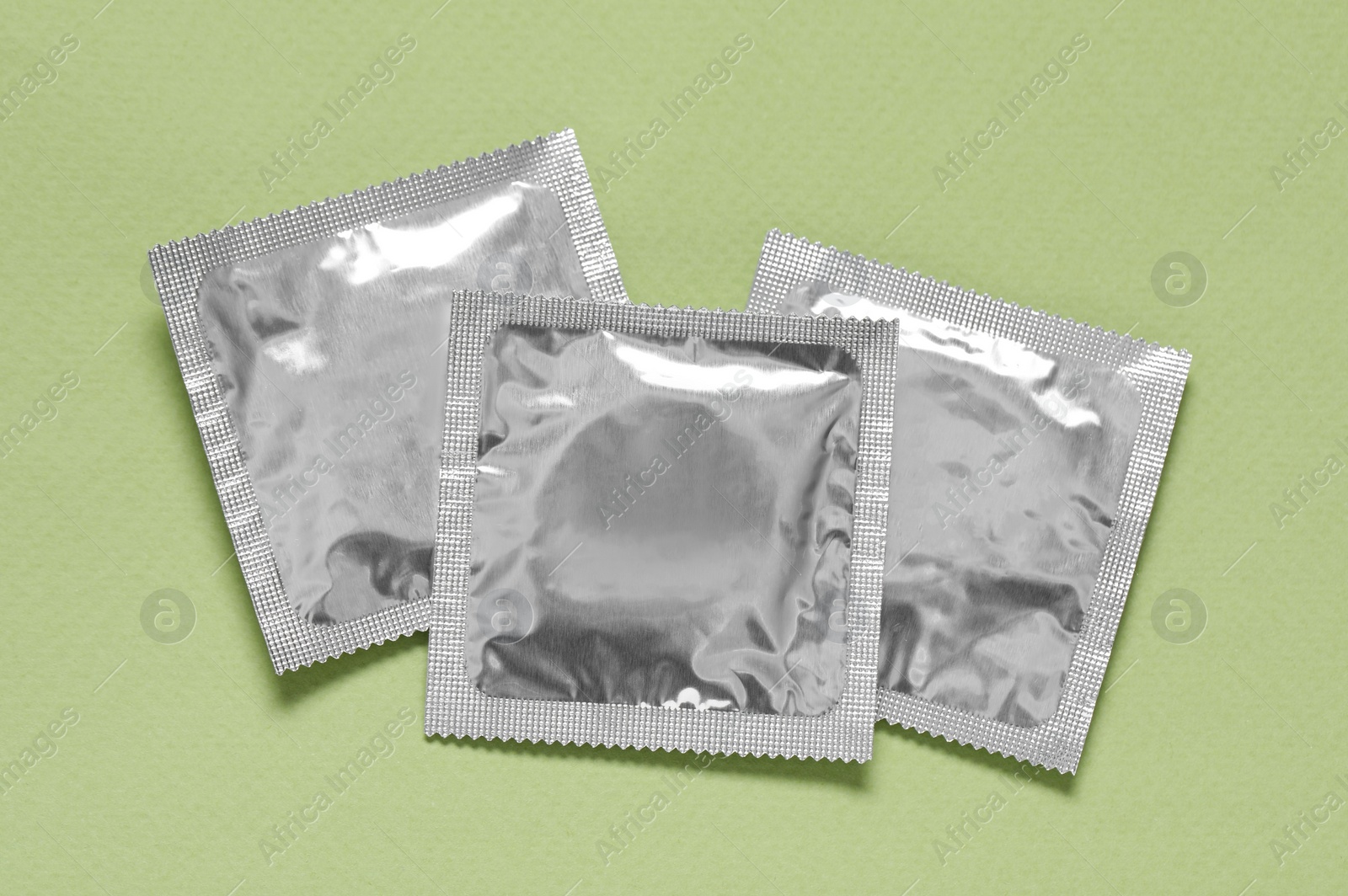 Photo of Condom packages on light green background, flat lay. Safe sex