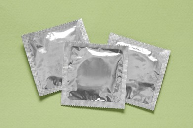 Photo of Condom packages on light green background, flat lay. Safe sex