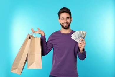 Photo of Portrait of happy young man with money and shopping bags on color background