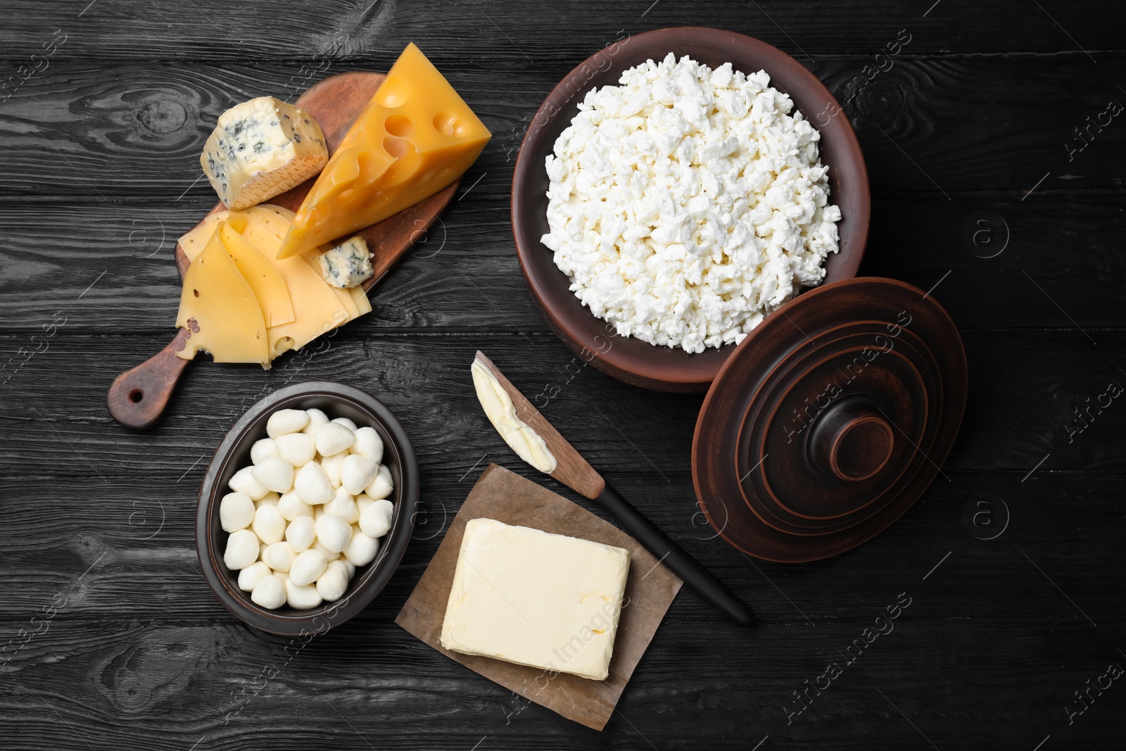 Photo of Clay dishware with fresh dairy products on black wooden table, flat lay