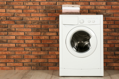 Photo of Modern washing machine with stack of towels near brick wall, space for text. Laundry day