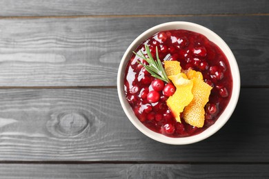 Photo of Fresh cranberry sauce, rosemary and orange peel in bowl on black wooden table, top view. Space for text