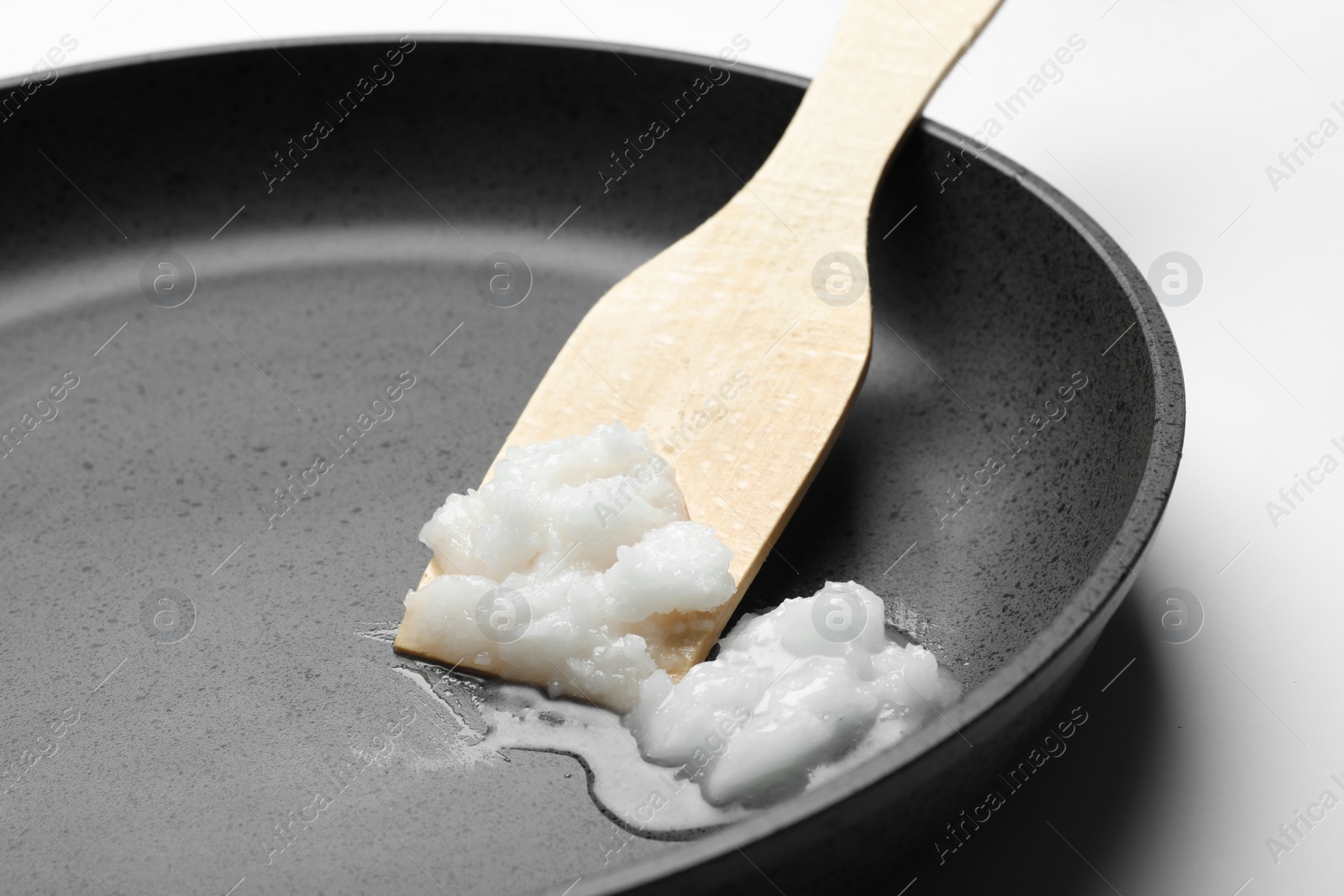 Photo of Frying pan with coconut oil and wooden spatula on white background, closeup. Healthy cooking