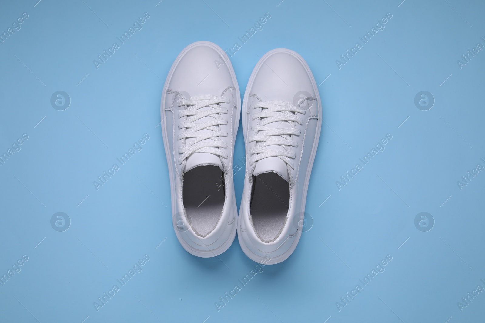 Photo of Pair of stylish white sneakers on light blue background, top view