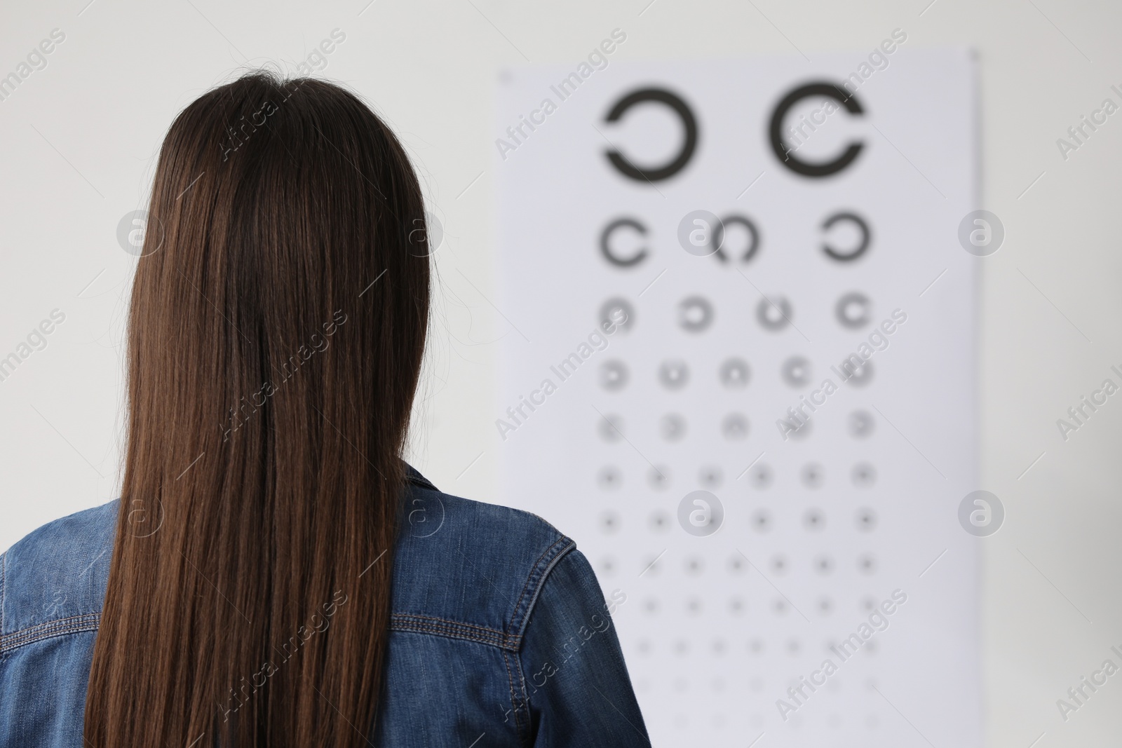 Photo of Eyesight examination. Young woman looking at vision test chart indoors, back view