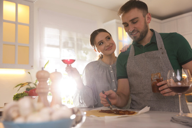Photo of Lovely young couple cooking pizza together in kitchen