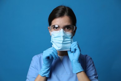 Doctor in protective mask, medical gloves and glasses against blue background