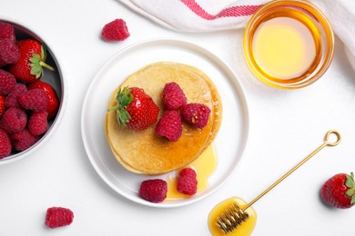 Tasty pancakes served with fresh berries and honey on white table, flat lay