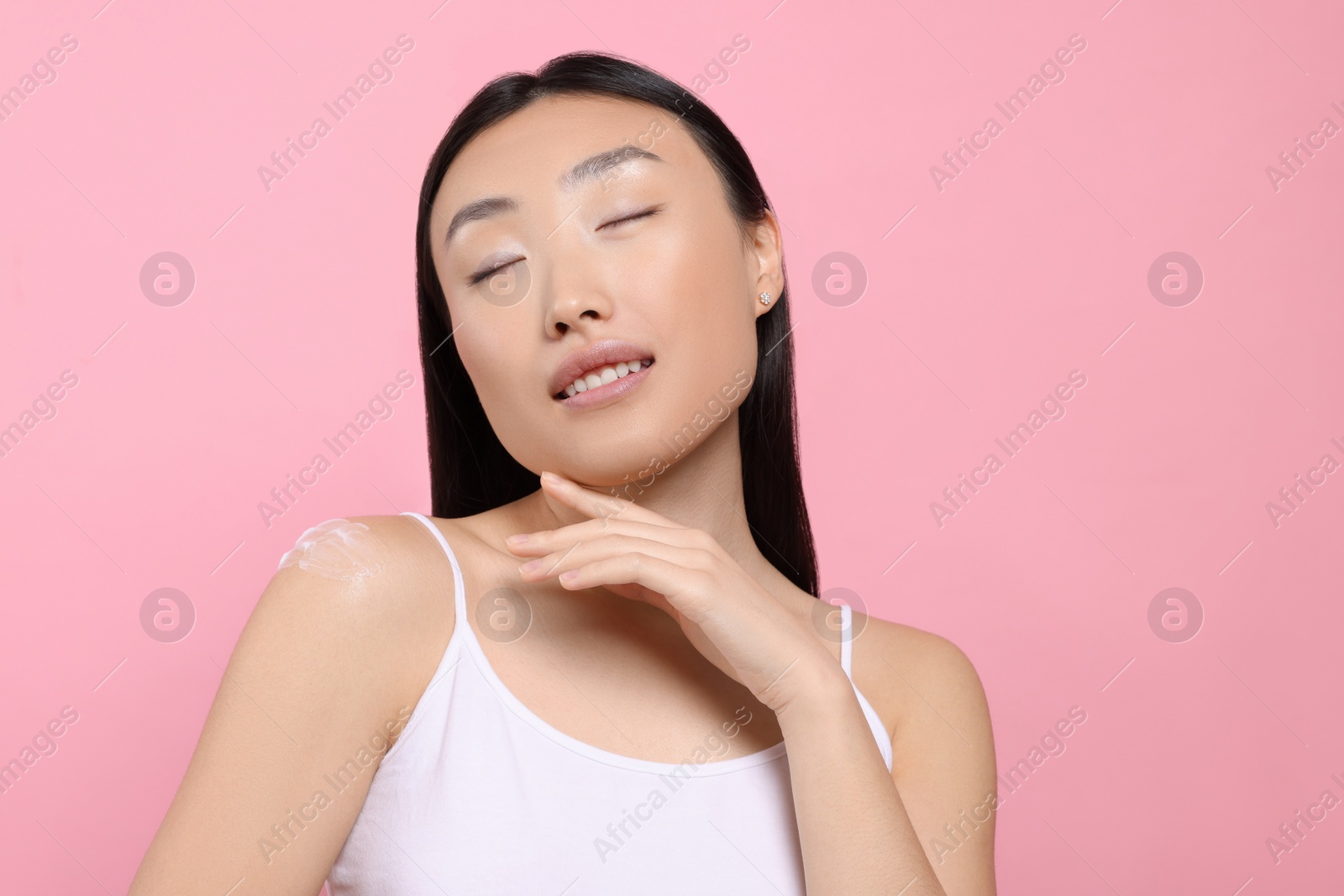 Photo of Beautiful young Asian woman with smear of body cream on shoulder against pink background
