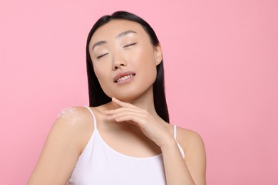 Photo of Beautiful young Asian woman with smear of body cream on shoulder against pink background