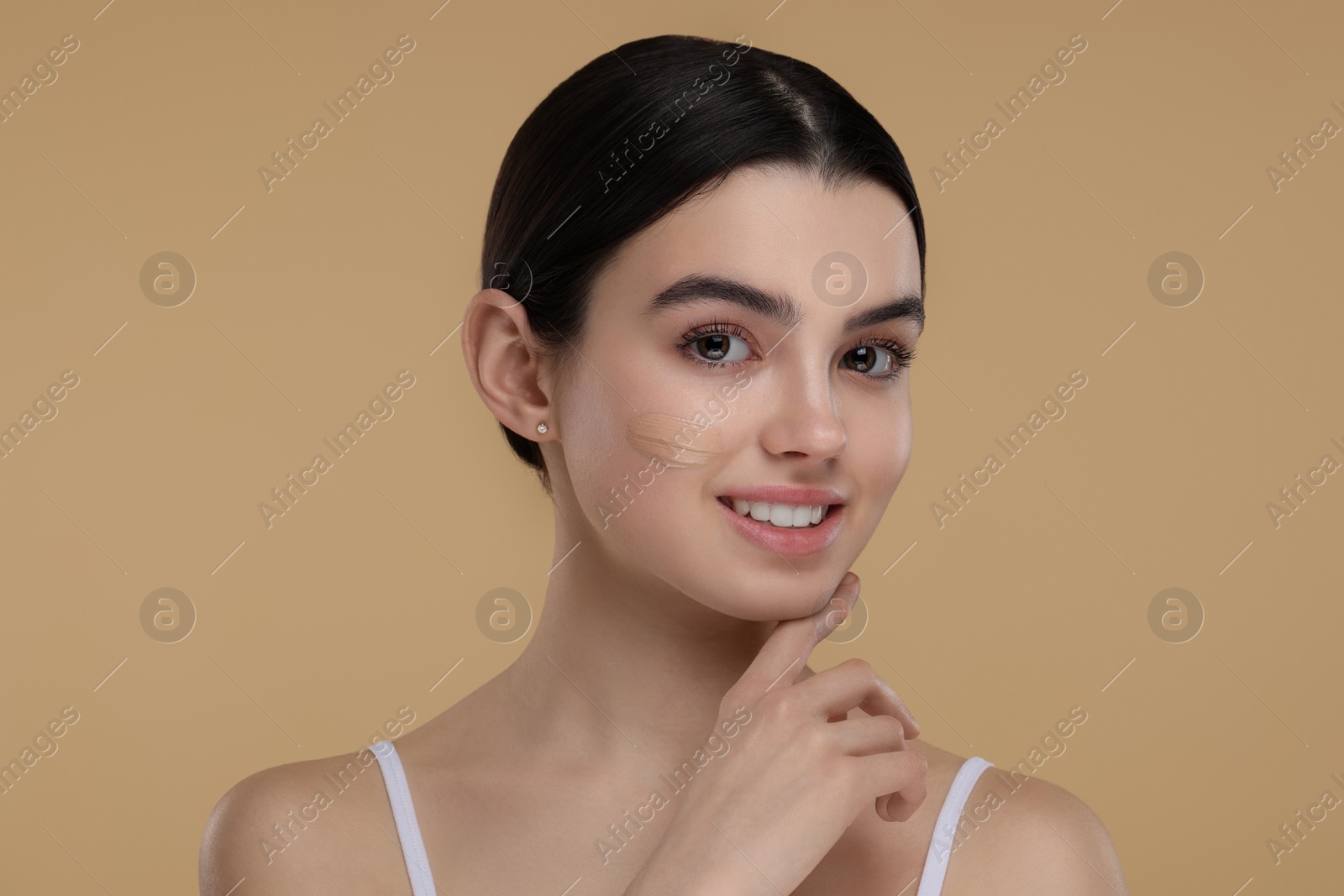 Photo of Teenage girl with swatch of foundation on face against beige background