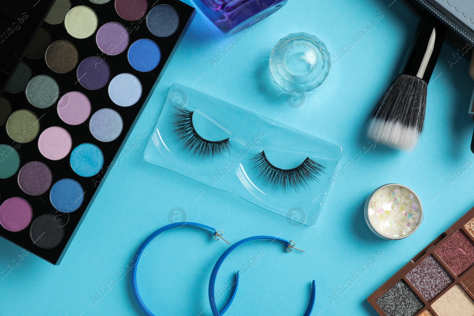 Photo of Set of makeup products and earrings on light blue background, flat lay