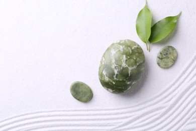 Photo of Zen garden stones and green leaves on white sand with pattern, flat lay. Space for text